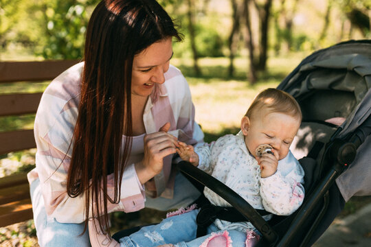 Mother caring for baby girl in stroller during sunny park walk