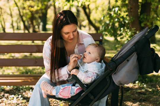 Mother caring for baby girl in stroller during sunny park walk