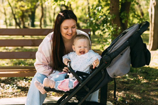 Smiling mother spending time with baby in stroller at sunny park
