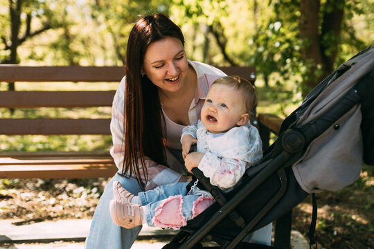Smiling mother spending time with baby in stroller at sunny park