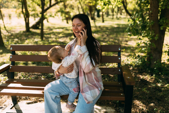 Happy young mother talking on smartphone while holding baby