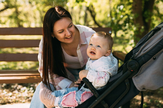 Mother caring for baby girl in stroller during sunny park walk