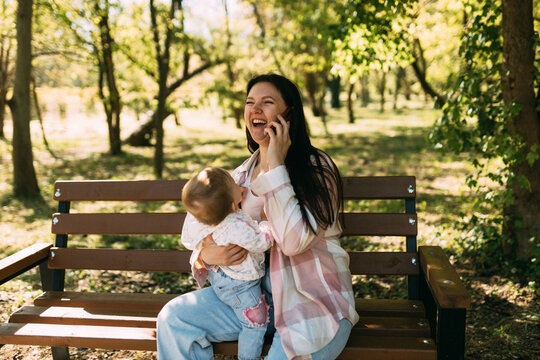 Happy young mother talking on smartphone while holding baby