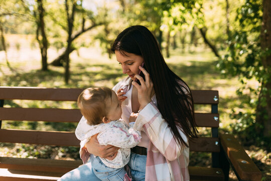 Young mother talking on smartphone while holding baby in park