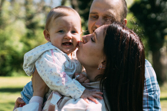 Young mother kissing adorable baby daughter while father standing