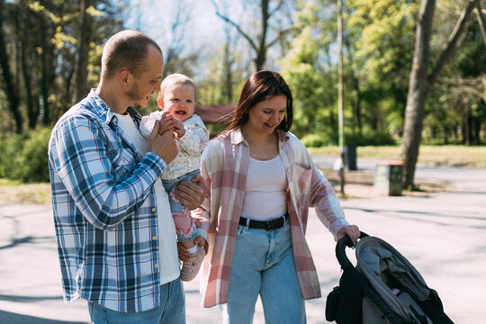 Young parents walking with smiling baby daughter and stroller in park