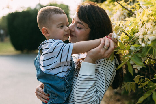 Happy mother holding laughing toddler near blooming flowers