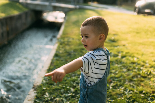 Curious toddler pointing at small stream in sunny park