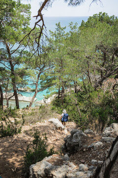 Hiker descends rugged trail to a turquoise cove