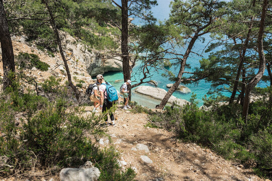 Three people hike a trail above a turquoise cove