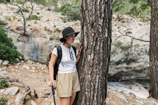 Female hiker in a bucket hat rests by a tree