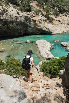 Woman hikes down a rocky path to a turquoise cove