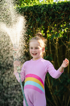 Happy, smiling child watering backyard in summer sunlight