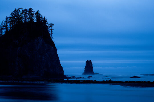 Silhouetted sea stacks on a moody blue coast