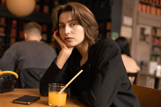 Young Woman in Black Blazer at Cafe Table looking at Camera