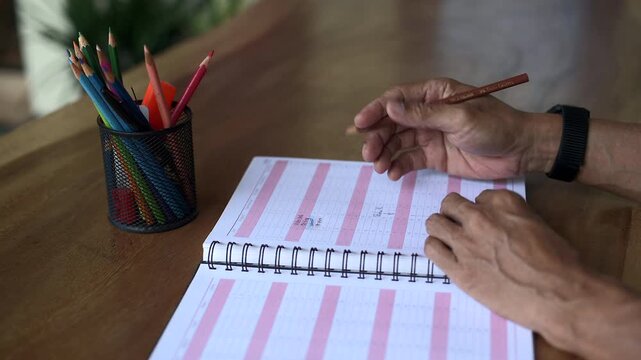 Asian male choosing color pencil and opening book page close up view. Shot from still camera static tripod