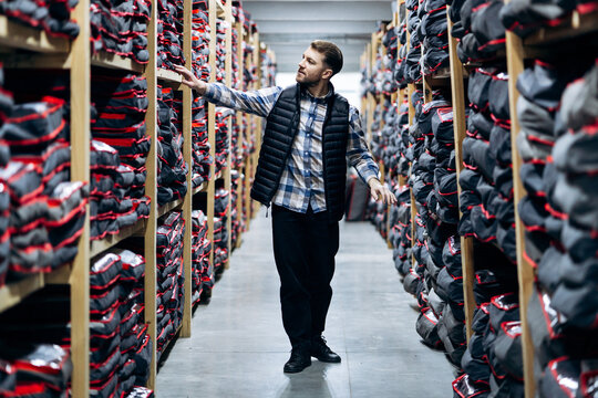Man managing stock control and organization in a retail warehouse, touching products on long wooden shelves