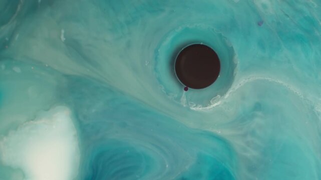 Abstract ink diffusion experiment showing purple and teal pigments mixing around a dark center. Top-down perspective of organic fluid textures for creative scientific backgrounds.