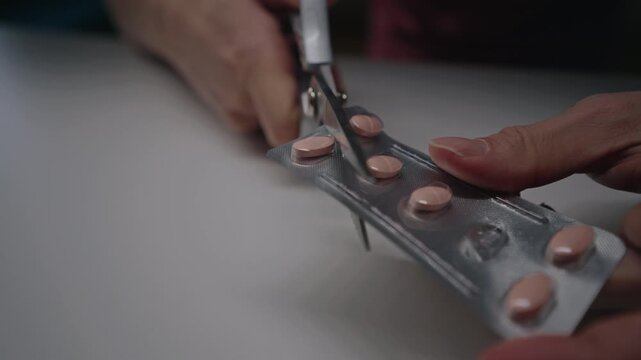 Closeup hands holding using scissors cutting single medication tablet from pharmaceutical blister pack, isolating one dose for daily treatment routine or preparing for travel, close-up, slow motion.