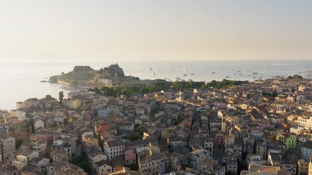 Slow drone panorama over Corfu Old Town at sunrise. Saint Spyridon Church, waterfront and Old Fortress bathed in golden morning light