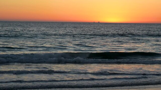 Gentle waves and distant ship silhouette at warm sunset Channelside Beach CA