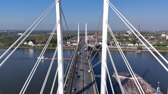 Forward aerial flight between bridge pylons above the road surface, showing cables, vehicles, and construction beyond.