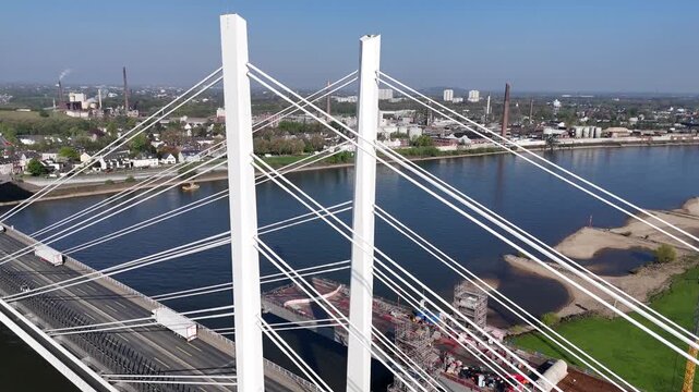 Centered drone flight over the bridge axis, revealing cable symmetry, roadway traffic, and Rheinhausen in the distance.