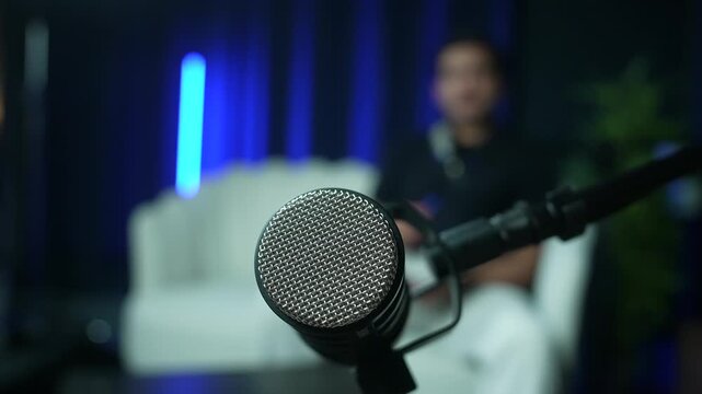 Close-up of microphone on boom arm with blurred person and sofa in studio setting