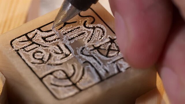 Close up shot of tool and artisan craftsman hands using a gouge to carve intricate details traditional chinese stone emblem stamp seal. Skilled craft worker hand-carving details at workshop