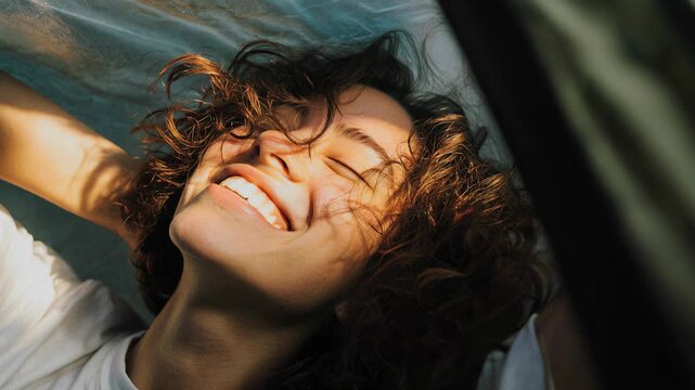 Joyful young woman with curly hair laughing with eyes closed in sunlight