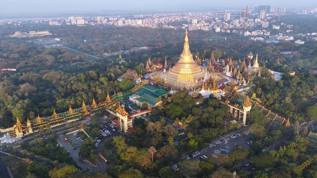 Aerial drone view at Shwedagon Pagoda, a golden stupa, surrounded by lush greenery and urban development in Yangon (Rangun), Myanmar (Burma), showcasing the city's blend of religious and modern life.