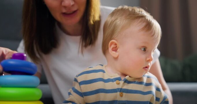Infant playing with colorful stacking rings while being supervised by an adult, demonstrating early childhood development and hand-eye coordination skills at home