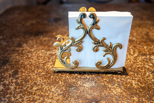 A beautifully crafted white paper bag with intricate gold floral designs and two round, gold-colored buttons stands on a small, rectangular, gold-topped base with a marble-like texture. The bag is