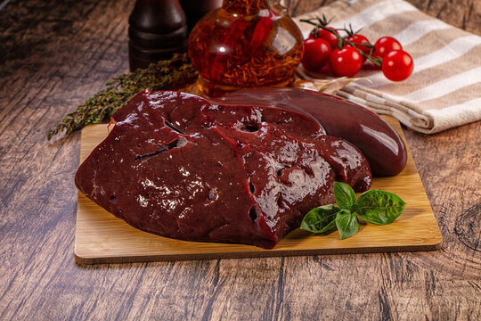 Raw beef liver on wooden cutting board with herbs and tomatoes for cooking