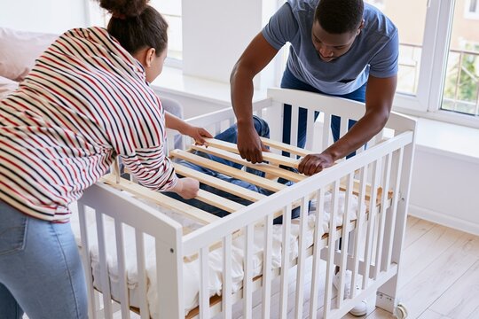 Parents installing mattress base inside baby crib together