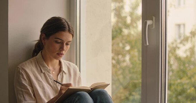 Woman writing in journal by window natural light