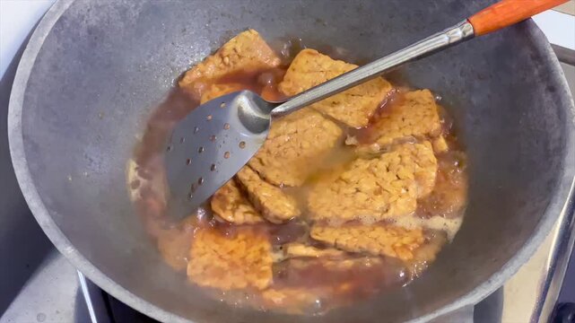 Cooking traditional indonesian braised tempeh known as tempe bacem in a wok