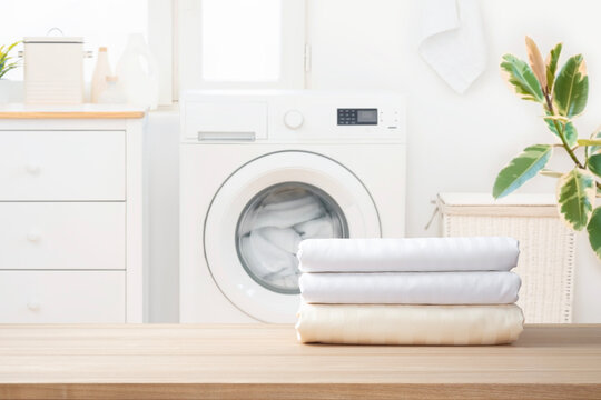 Clean folded textile bedding on wooden table over blurred rustic laundry room interior background