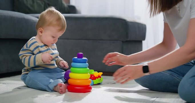 A toddler playing on the floor with colorful stacking rings and a toy car while an adult interacts nearby, highlighting early childhood development and parent-child bonding in a home environment