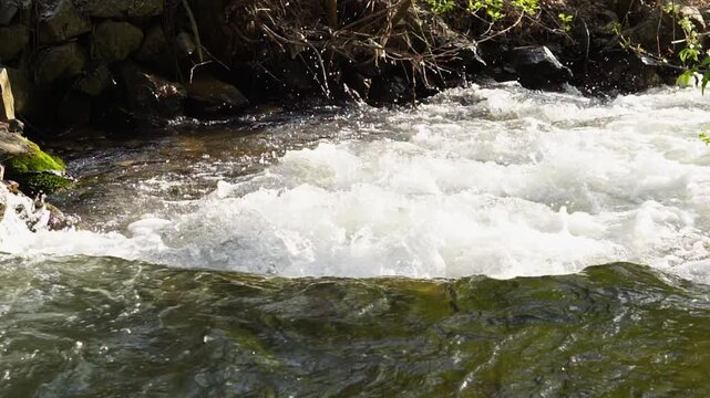 A close-up video of the surface of a turbulent mountain river with clear water, filmed at 4x slower, and view from behind along the current, from above. Soothing nature footage, 30 fps, Full HD