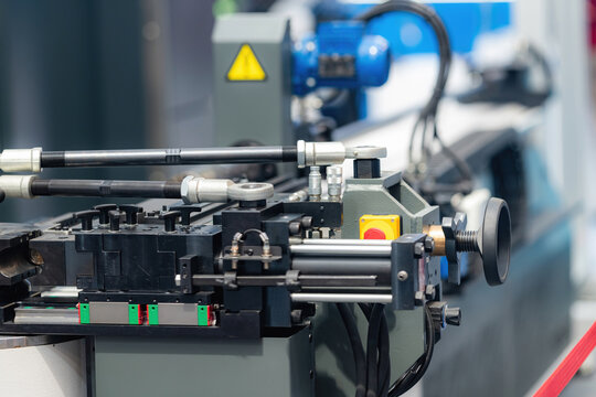 Heavy duty industrial tube or pipe bending machine with hydraulic components and safety markings demonstrated at an indoor manufacturing technology exhibition,  