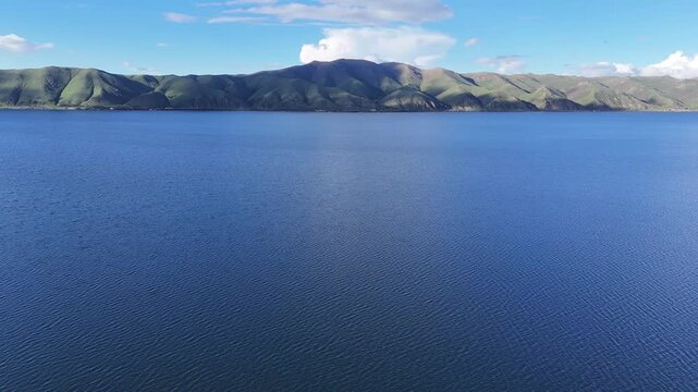 4K Drone Aerial View of Calm Mountain Lake With Green Hills Beneath Atmospheric Clouds.