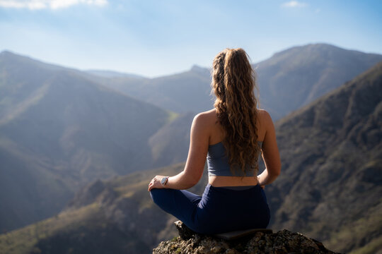 Female traveler meditating in the lotus position on a mountain viewpoint, back view. The concept of wellness and mindfulness in a highland landscape.
