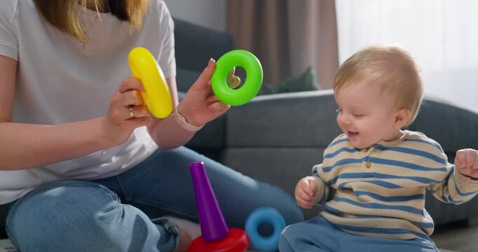 Young toddler playing with colorful stacking rings and toy trucks on a soft mat while being engaged by a caregiver in a cozy living room setting during daytime