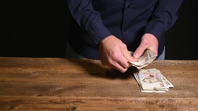 man reads banknotes of 100 Ukrainian hryvnias on wooden table. cash accounting. businessman recalculates profits, concept of small business in Ukraine. income, savings and finance.