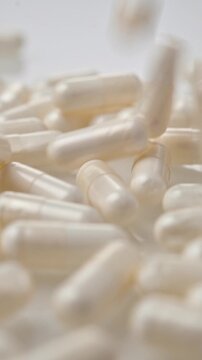 White supplement capsules fall onto glossy surface in vertical macro shot with soft focus for healthcare product concept
