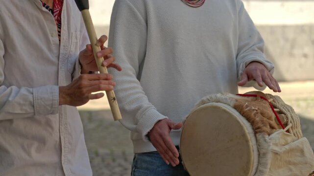 Slow motion close up of two people performing traditional Colombian music, playing a leather drum and a Guajira flute. Cultural heritage scene with no audio.