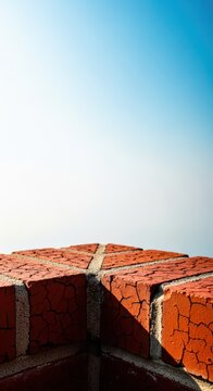 Weathered red clay bricks forming the edge of an old building parapet wall against a bright sky background in harsh midday light, sky, detail, brick