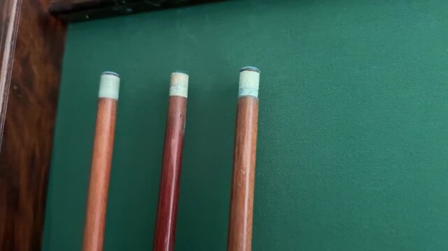 tree billiard cues against green wall, minimal sports equipment close up