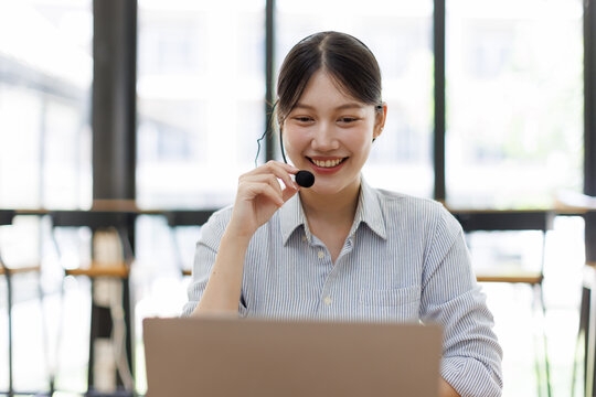 Smiling woman working at a laptop with a headset, providing excellent customer service and support from a call center or telemarketing office, communicating with clients